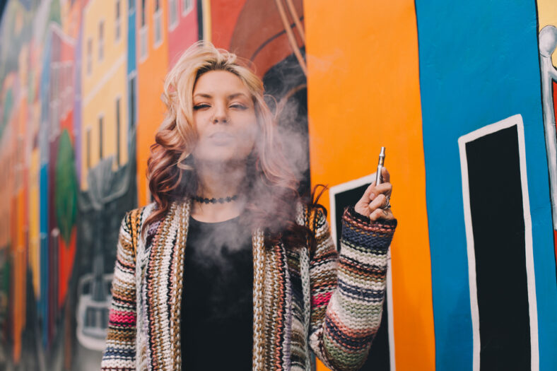 woman with a vap pen, cloud of smoke, colorful street